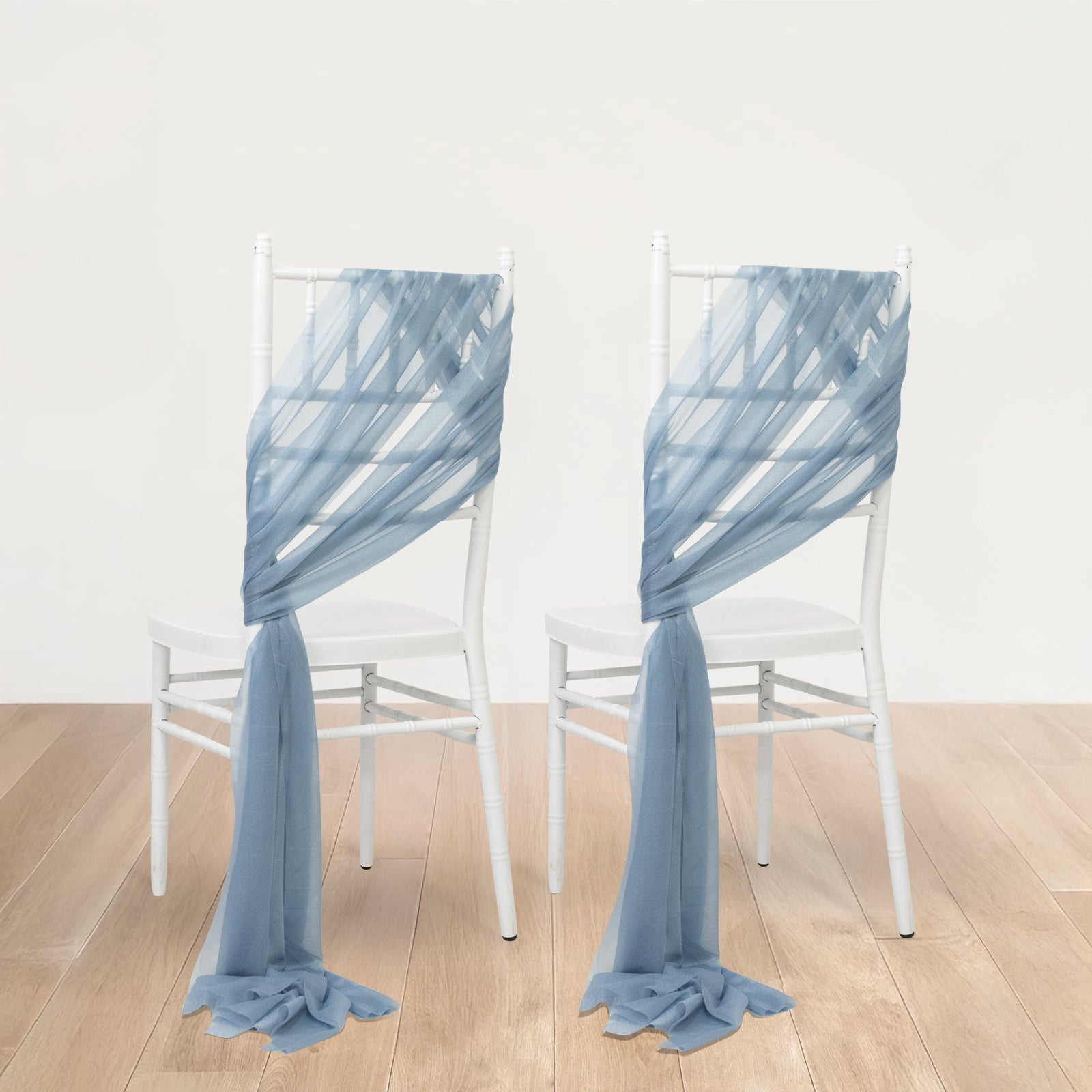 Dusty blue sheer chair drapes elegantly arranged on white chairs.