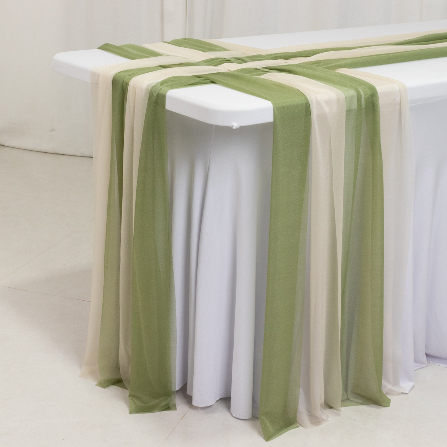 Dusty sage green and beige sheer table runners draped elegantly on a table.