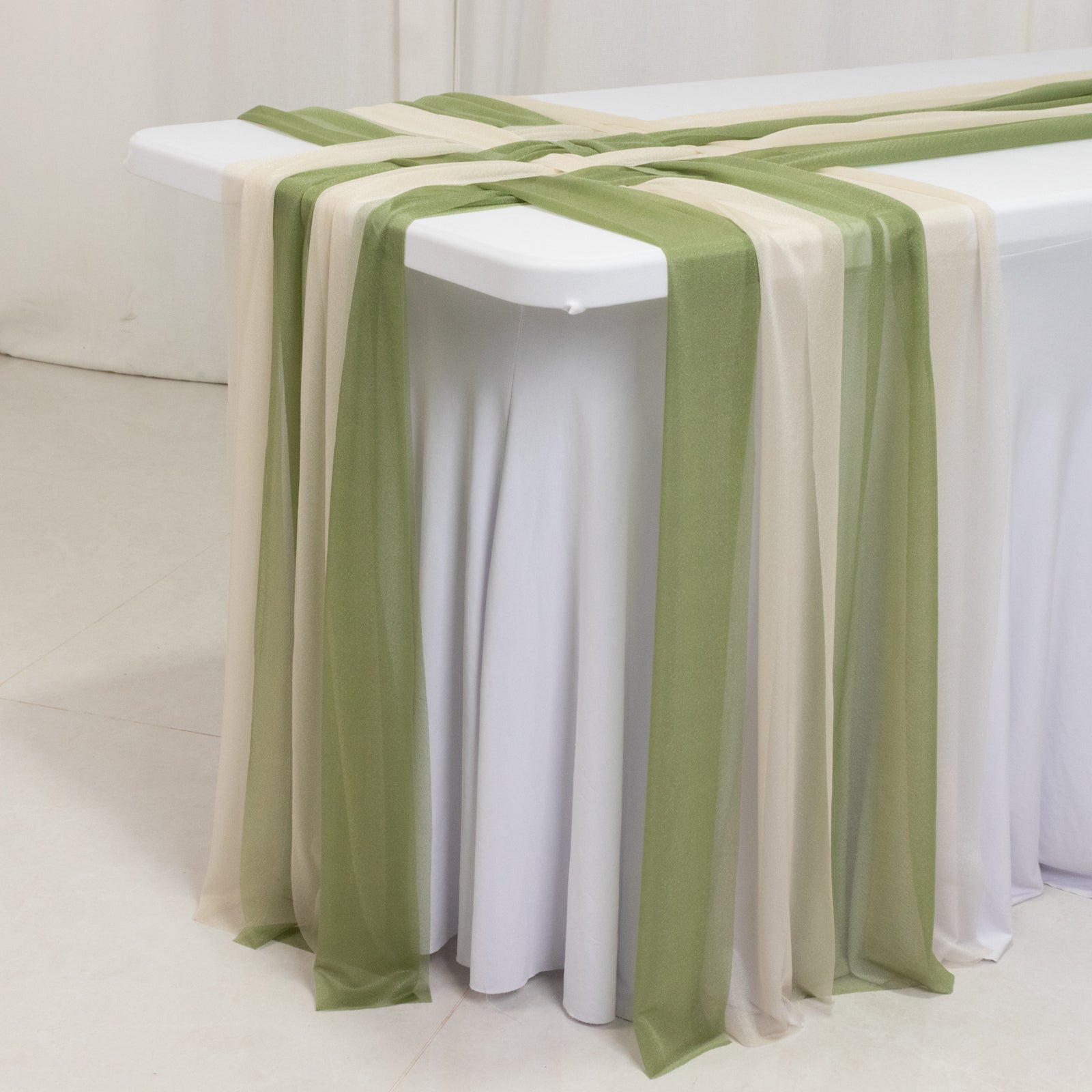 Dusty sage green and beige sheer table runners draped elegantly on a table.