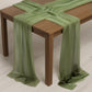 Dusty sage green sheer table runner draped elegantly over a wooden table.