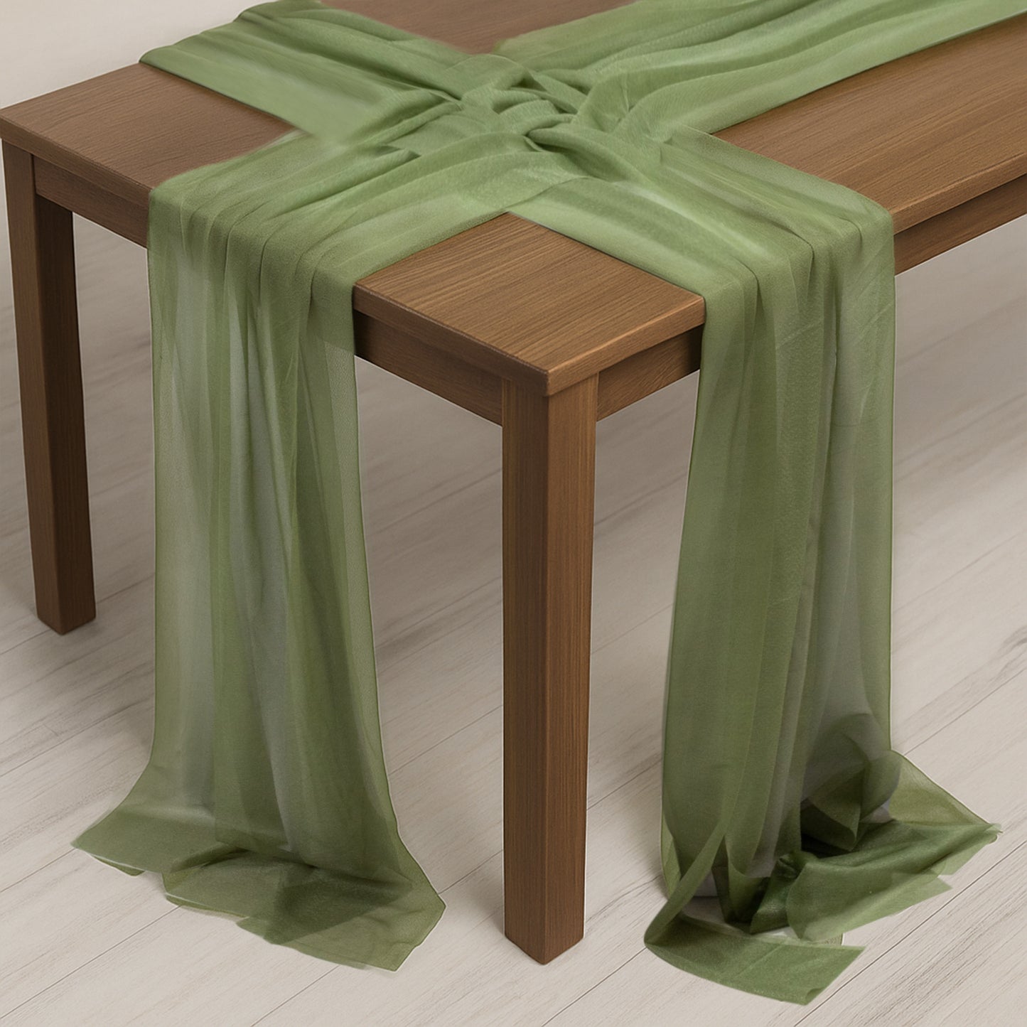 Dusty sage green sheer table runner draped elegantly over a wooden table.