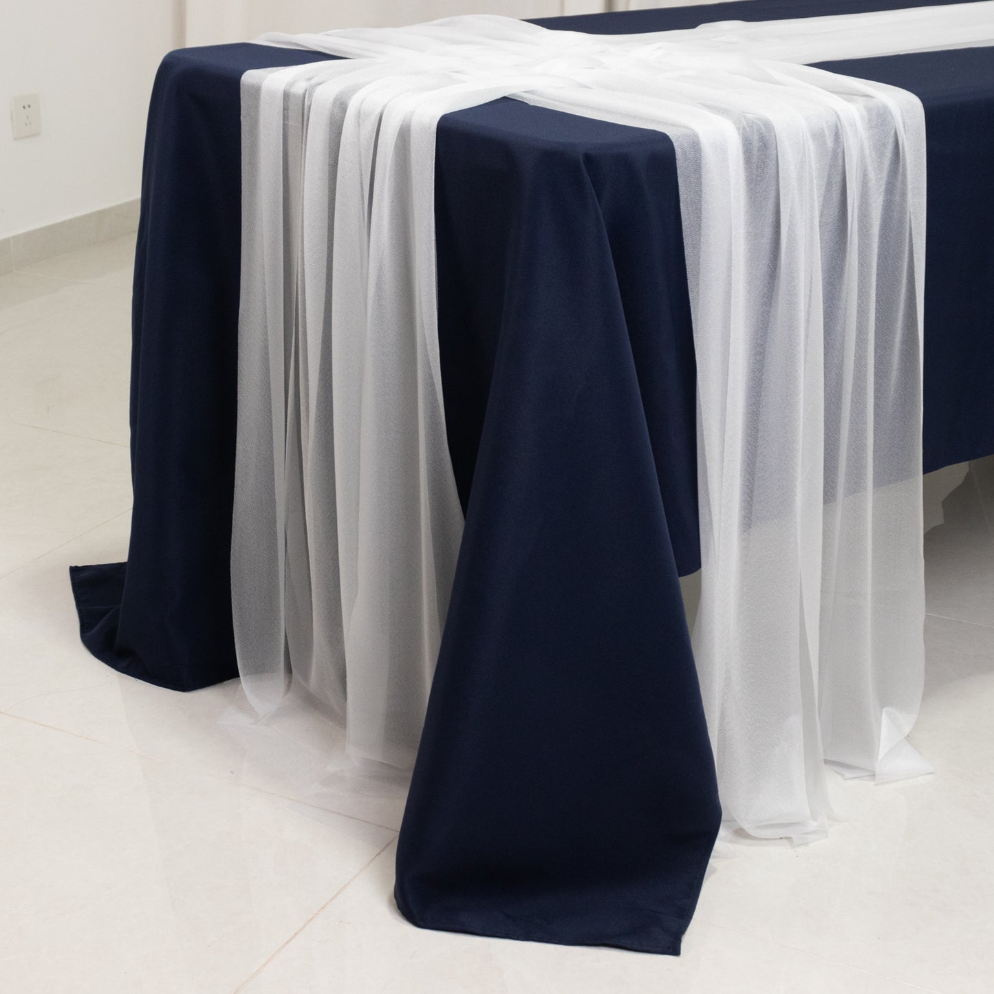 White sheer table runners draping over a navy blue table.