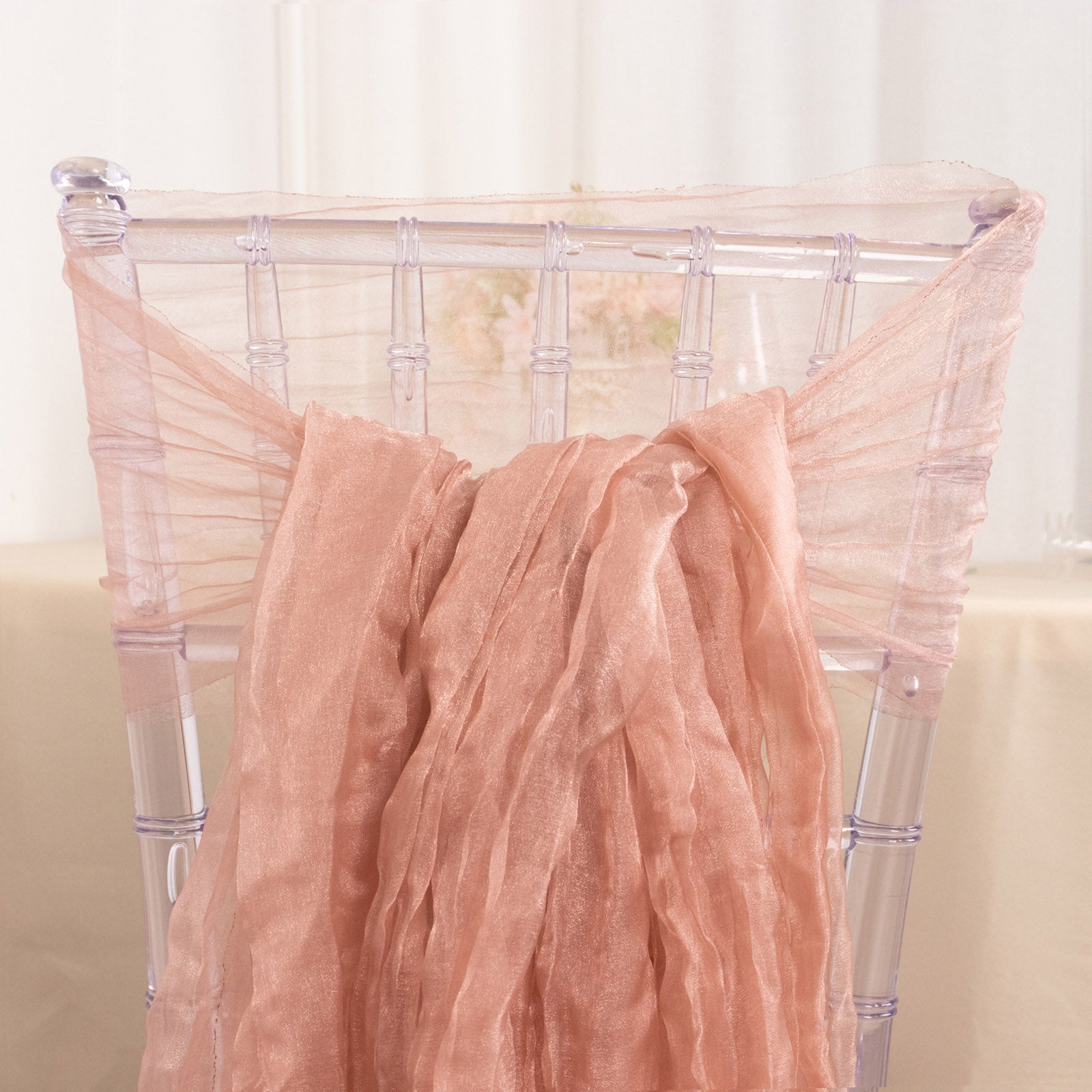 Dusty rose sheer crinkled organza chair sash on a transparent chair.