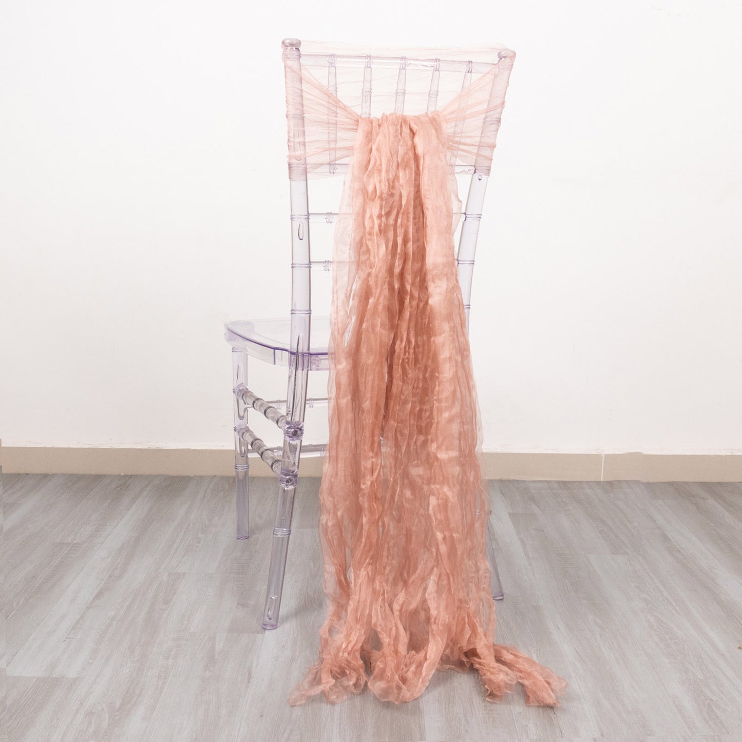 Dusty rose sheer crinkled organza chair sash draped on a clear chair.