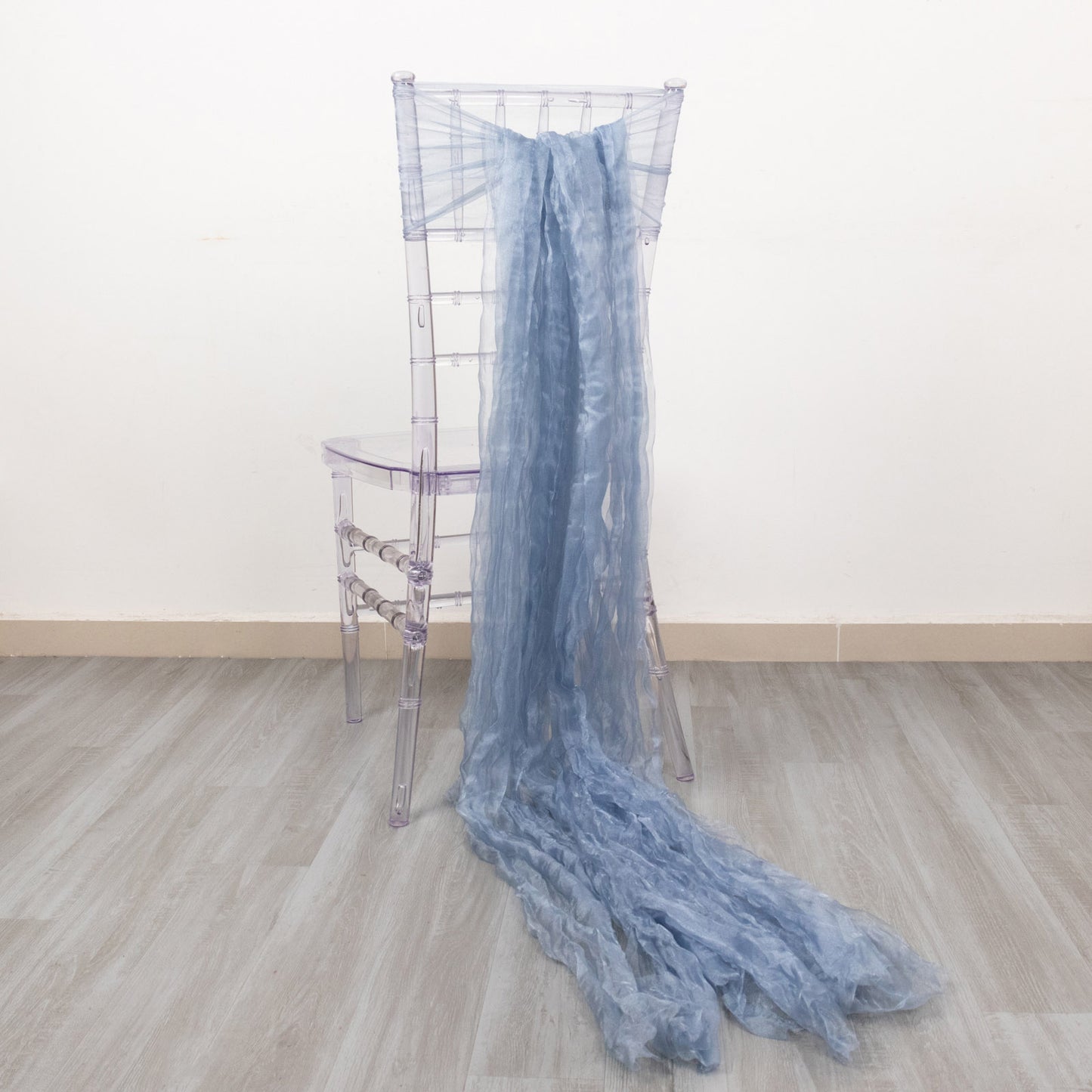 Dusty blue sheer crinkled organza chair sashes draped on a clear chair.