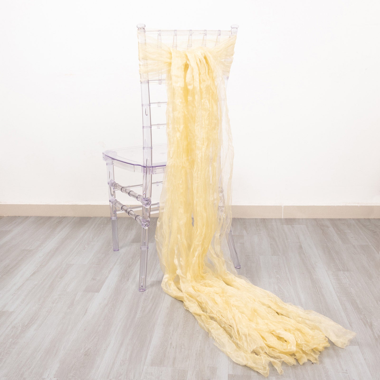 Champagne sheer crinkled organza chair sash draped on a clear chair.