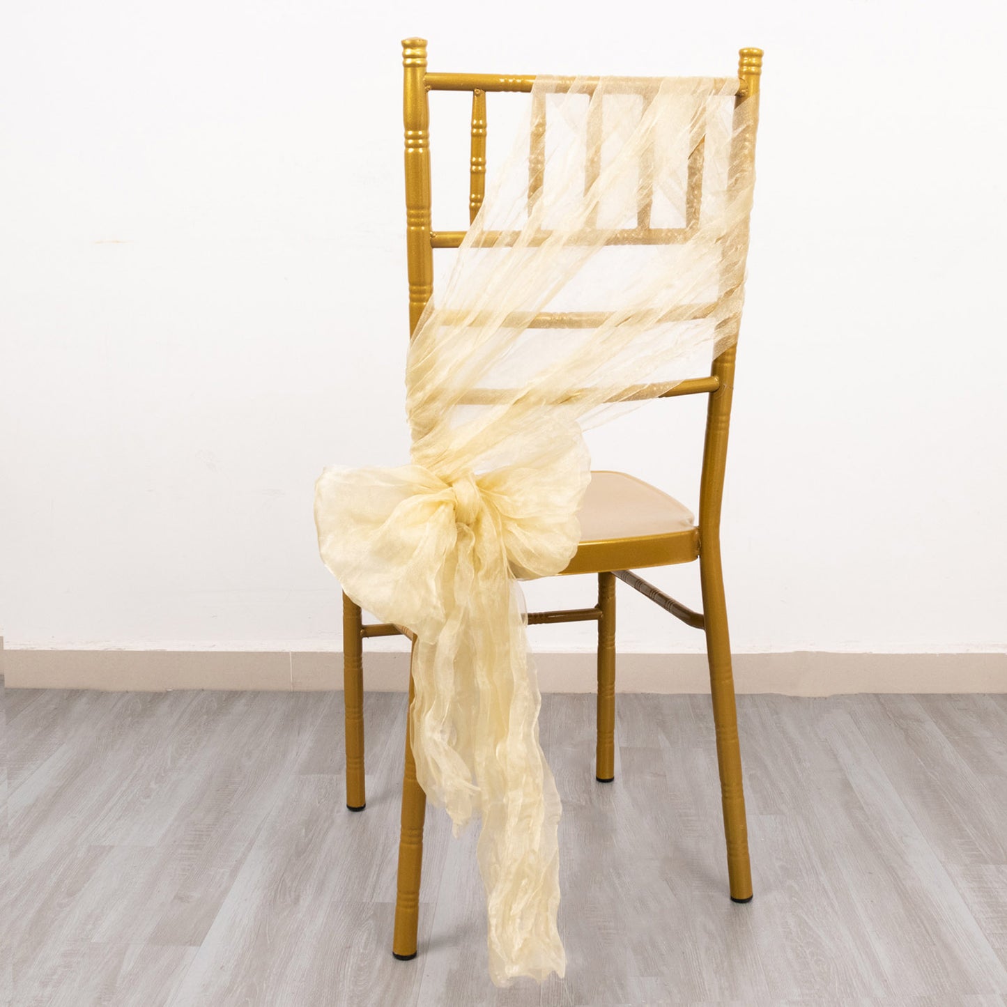 Champagne sheer crinkled organza chair sash tied on a gold chiavari chair.