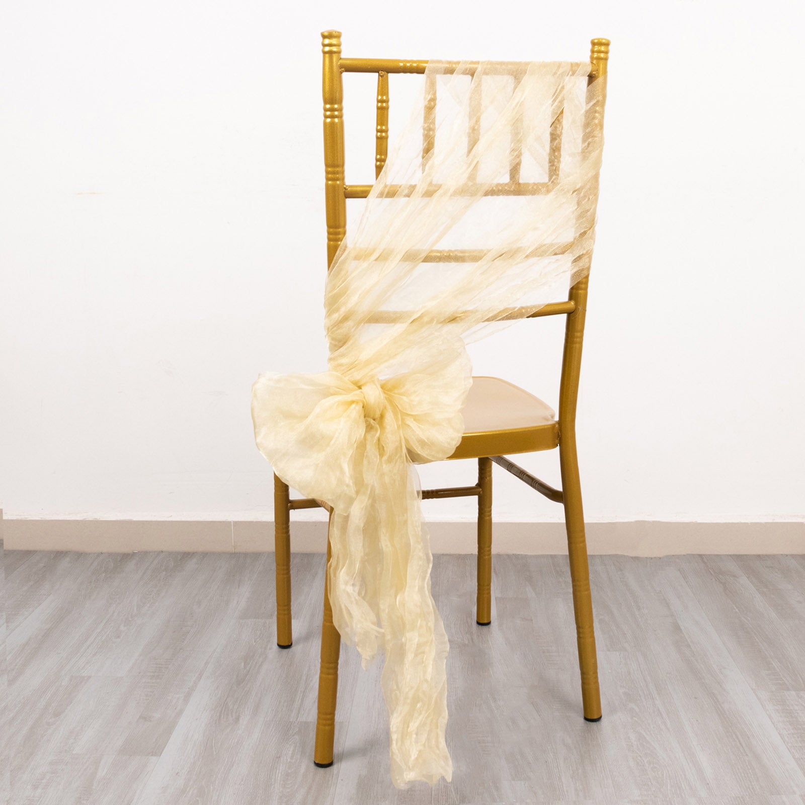Champagne sheer crinkled organza chair sash tied on a gold chiavari chair.