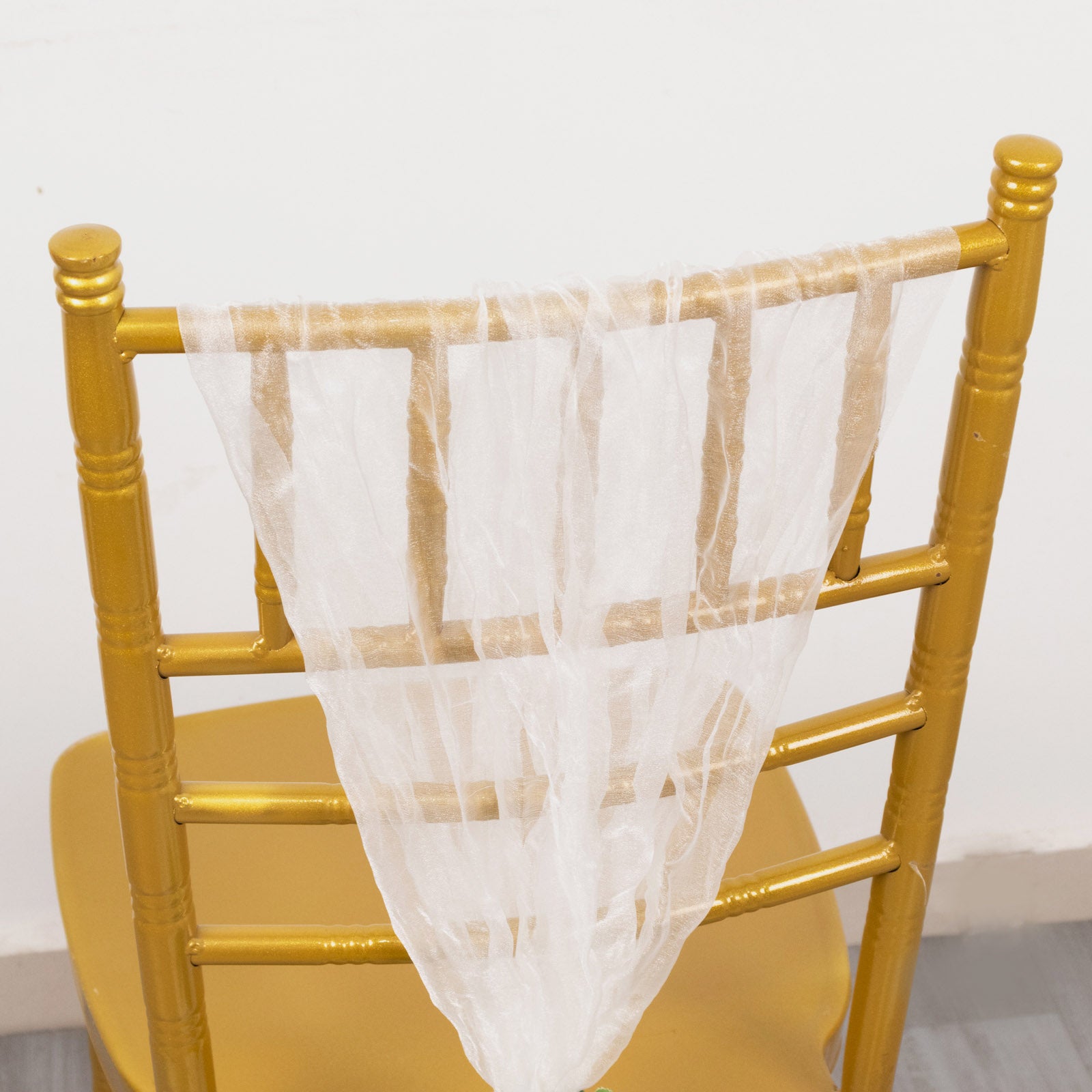White sheer crinkled organza chair sash draped over a gold chair.