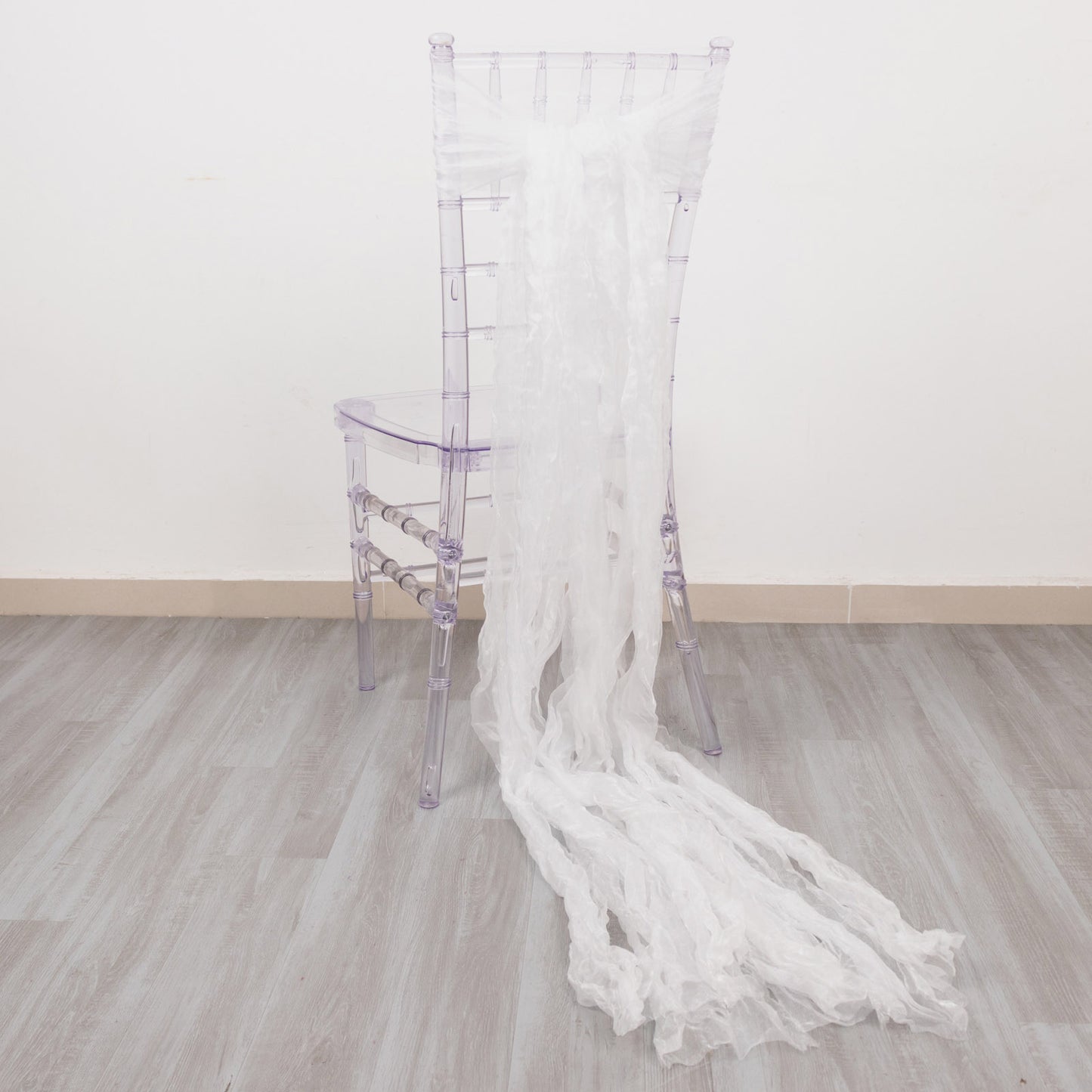 White sheer crinkled organza chair sashes elegantly draping a clear chair.