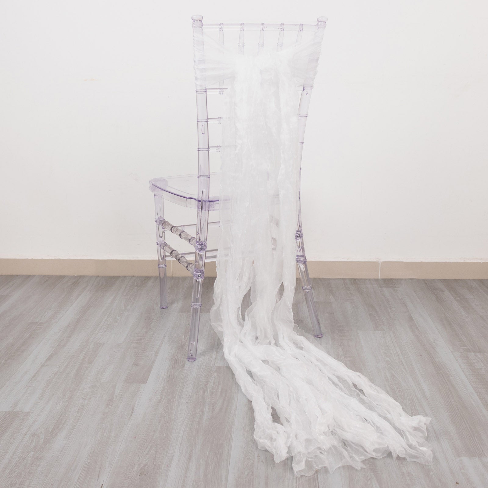 White sheer crinkled organza chair sashes elegantly draping a clear chair.