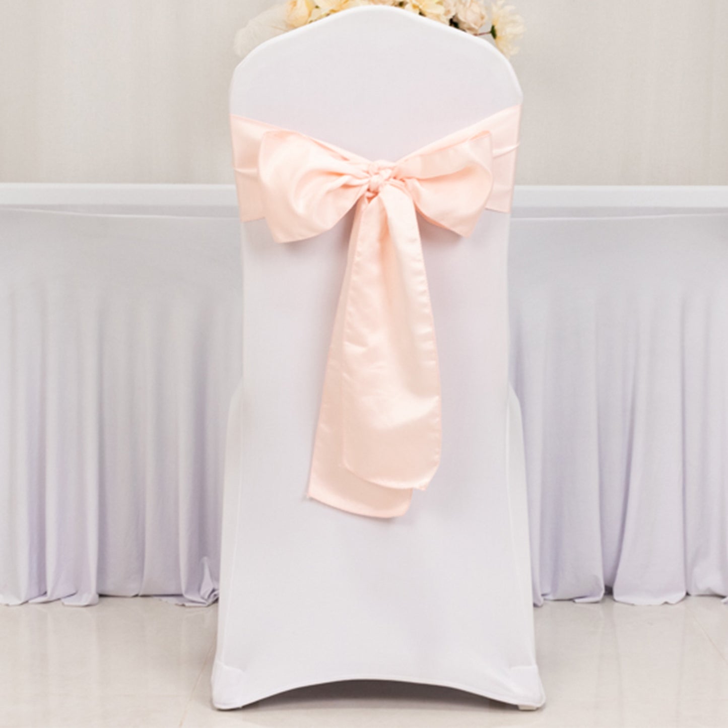 Blush satin chair sash with bow on a white chair.