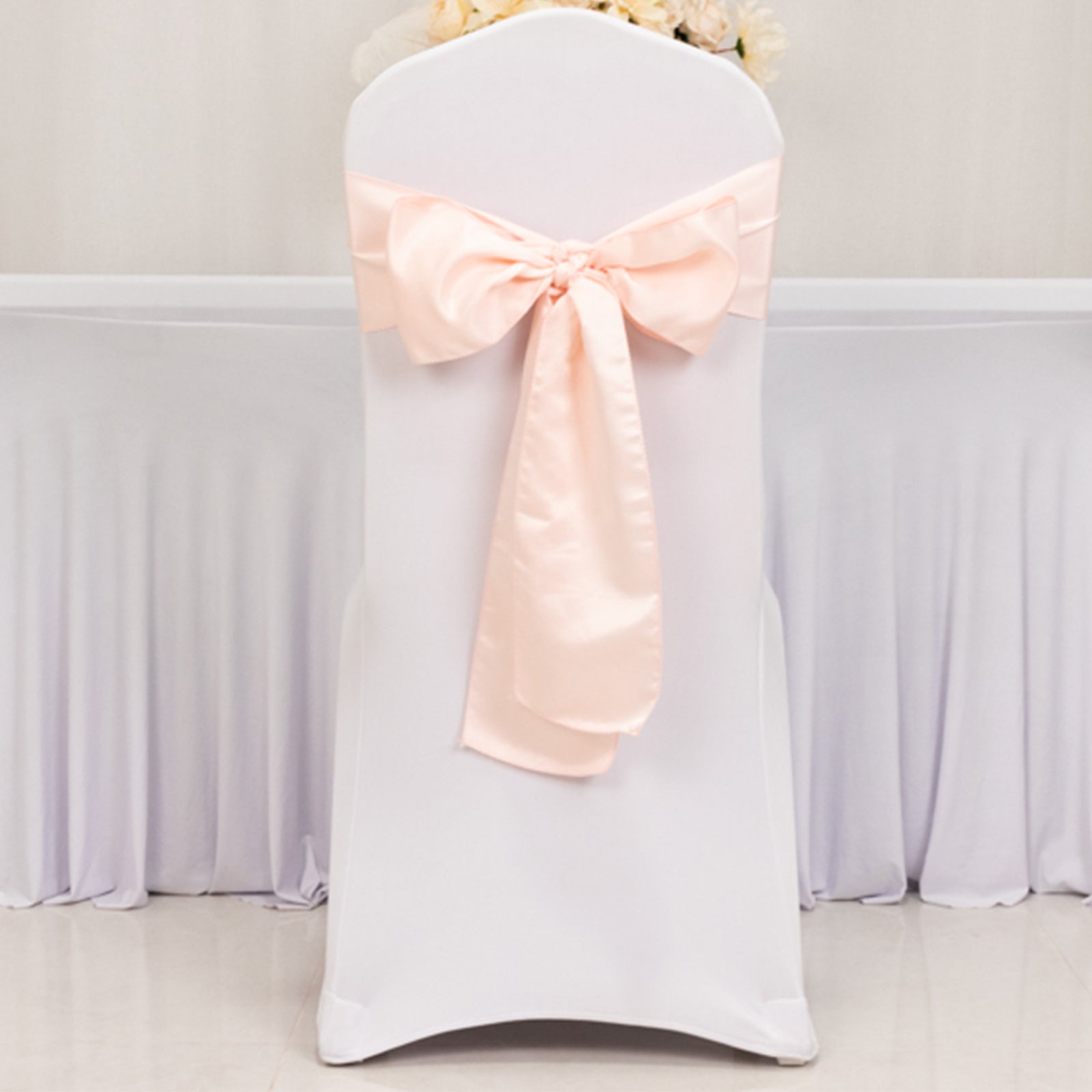 Blush satin chair sash with bow on a white chair.