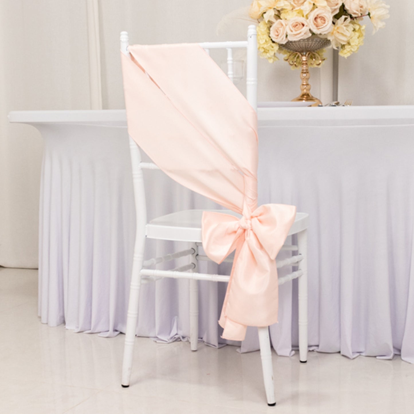Blush satin chair sash with bow on a white chair at an elegant event.