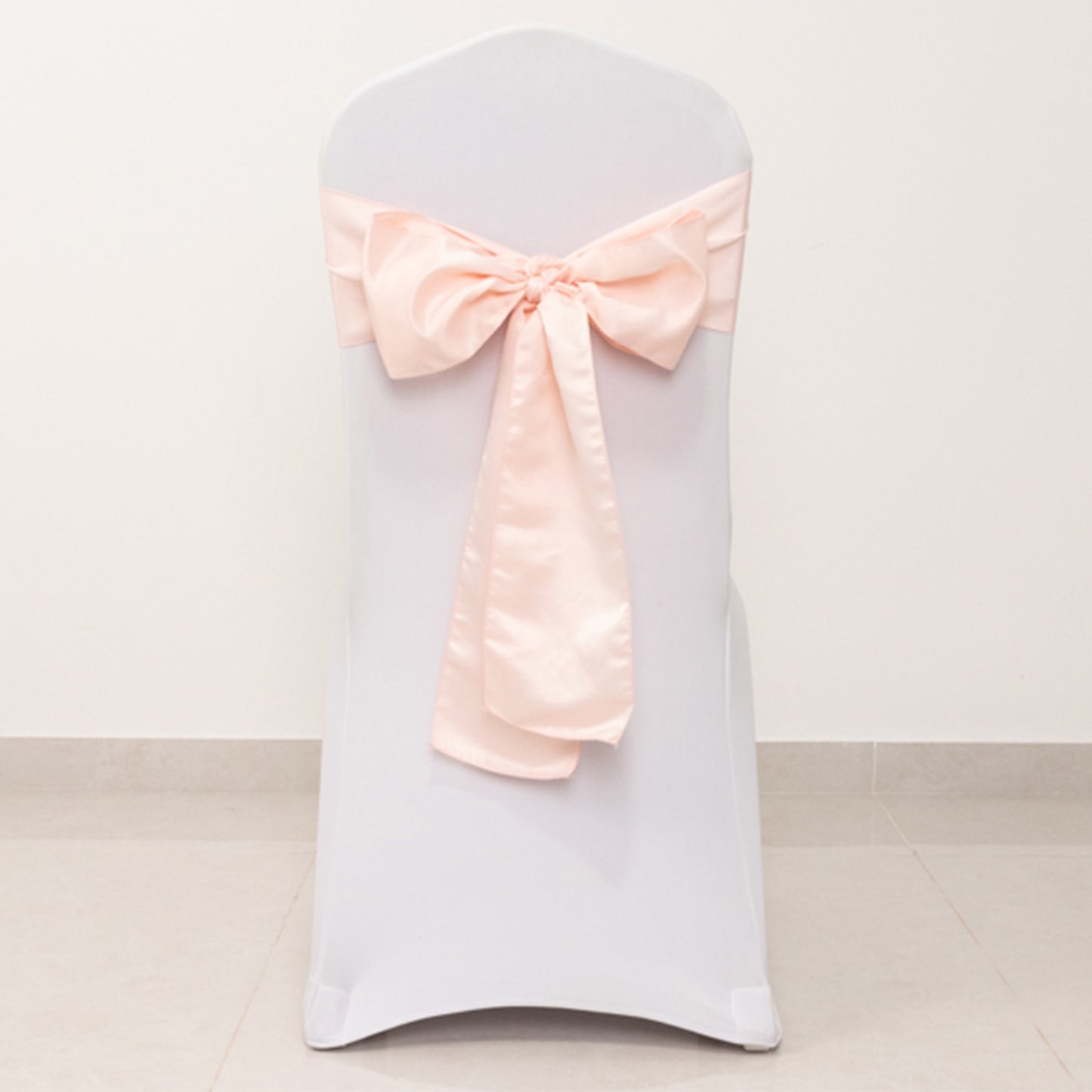 Blush satin chair sash bow tied on a white chair.