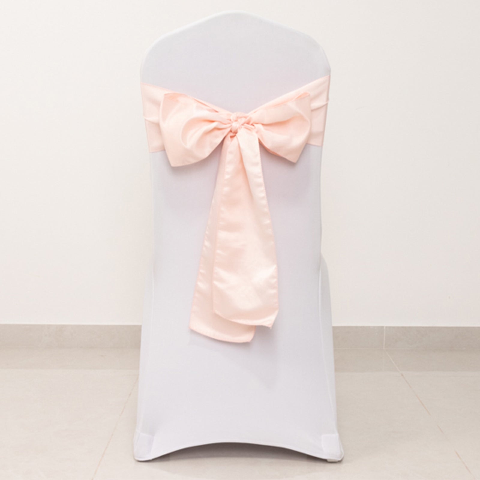 Blush satin chair sash bow tied on a white chair.