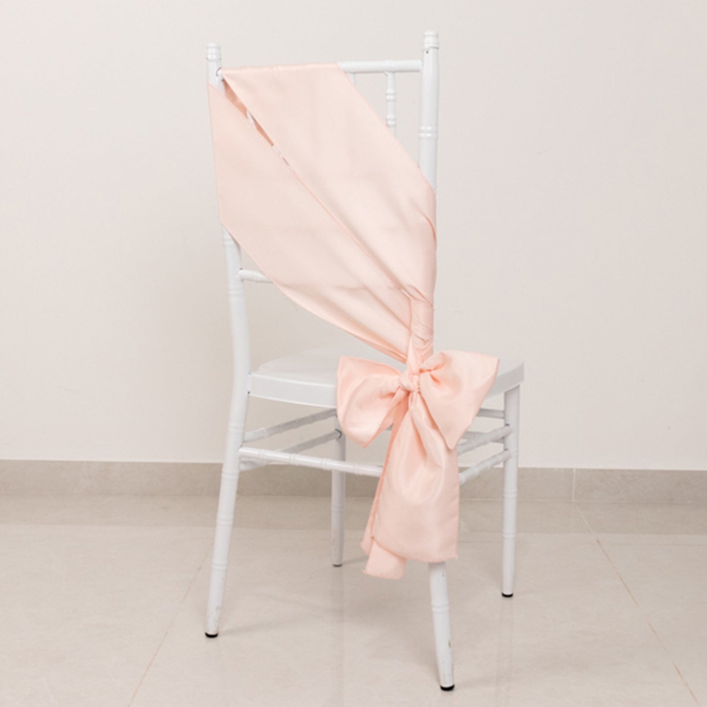 Blush satin chair sash bow on a white chair.