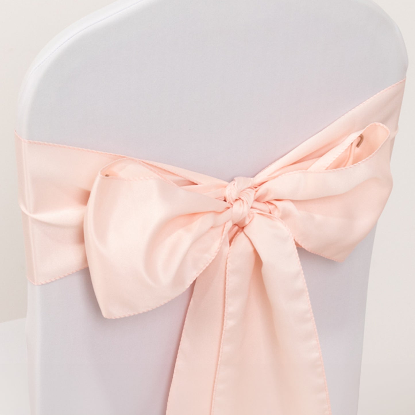 Blush satin chair sash bow on a white chair.