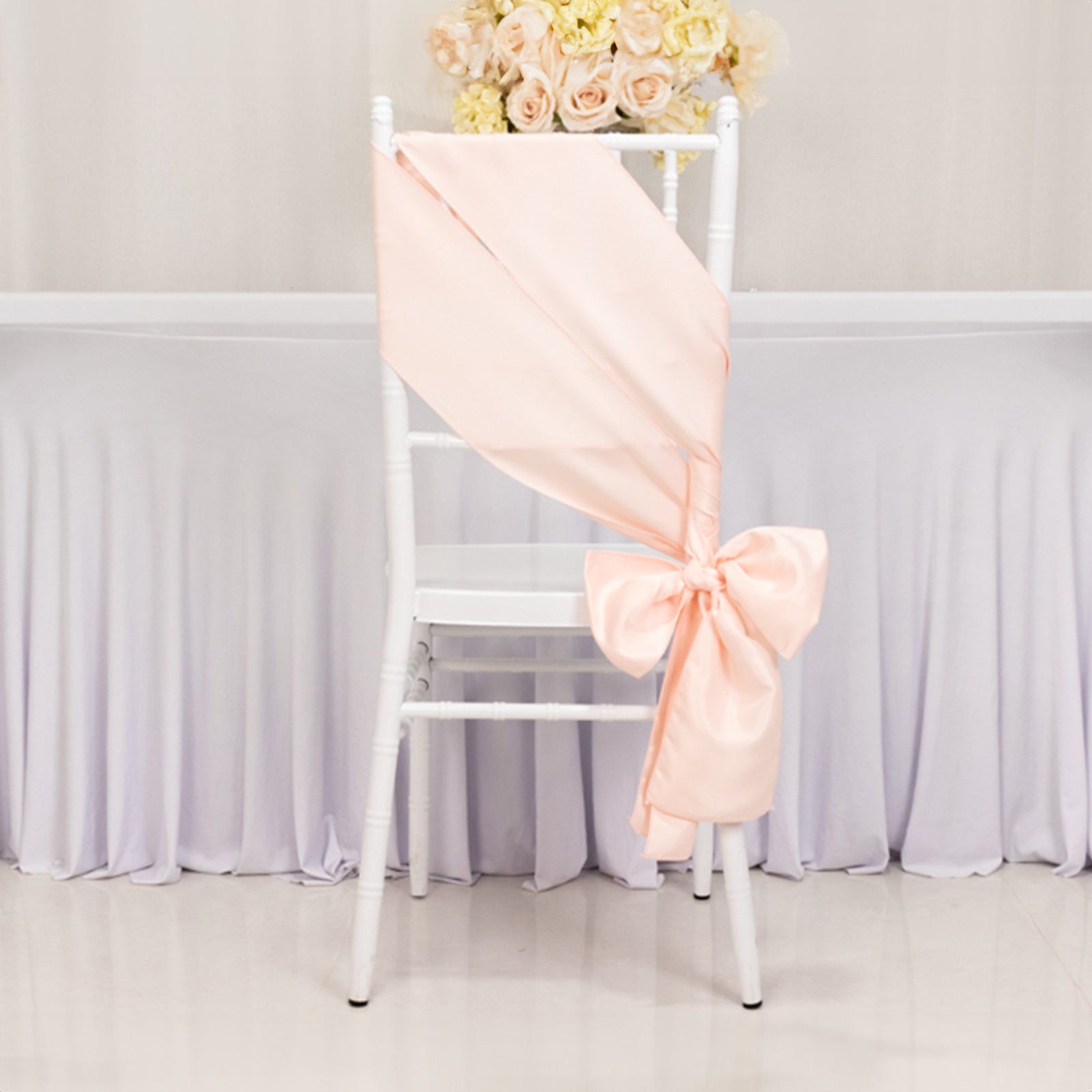Blush satin chair sash with bow draped on a white chair.