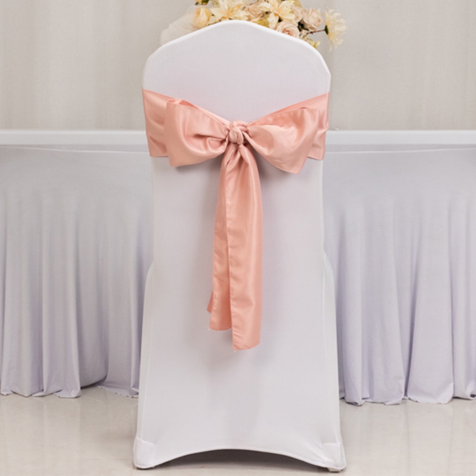 Dusty rose satin chair sash bow on a white chair.