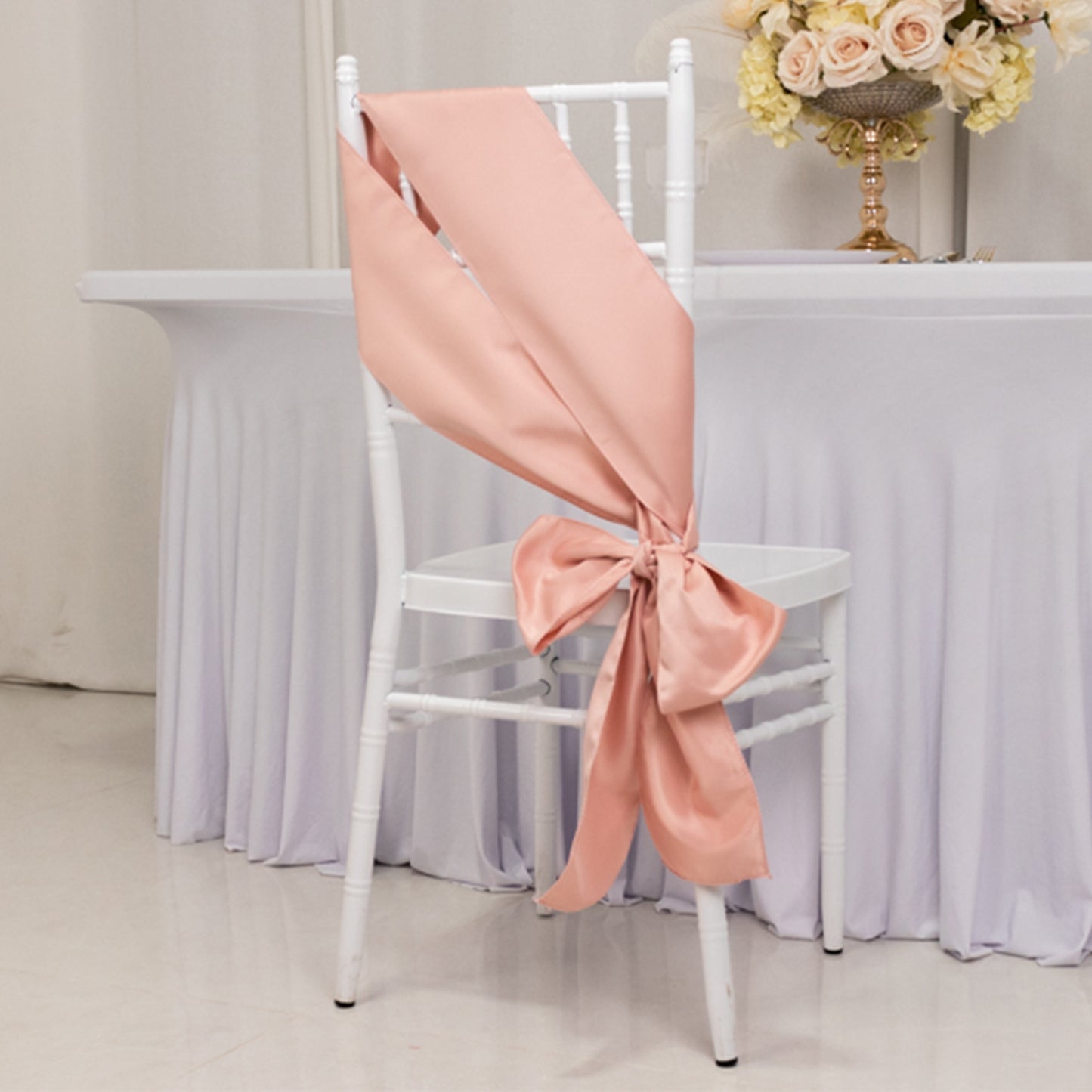Dusty rose satin chair sash tied in a bow on a white chair.