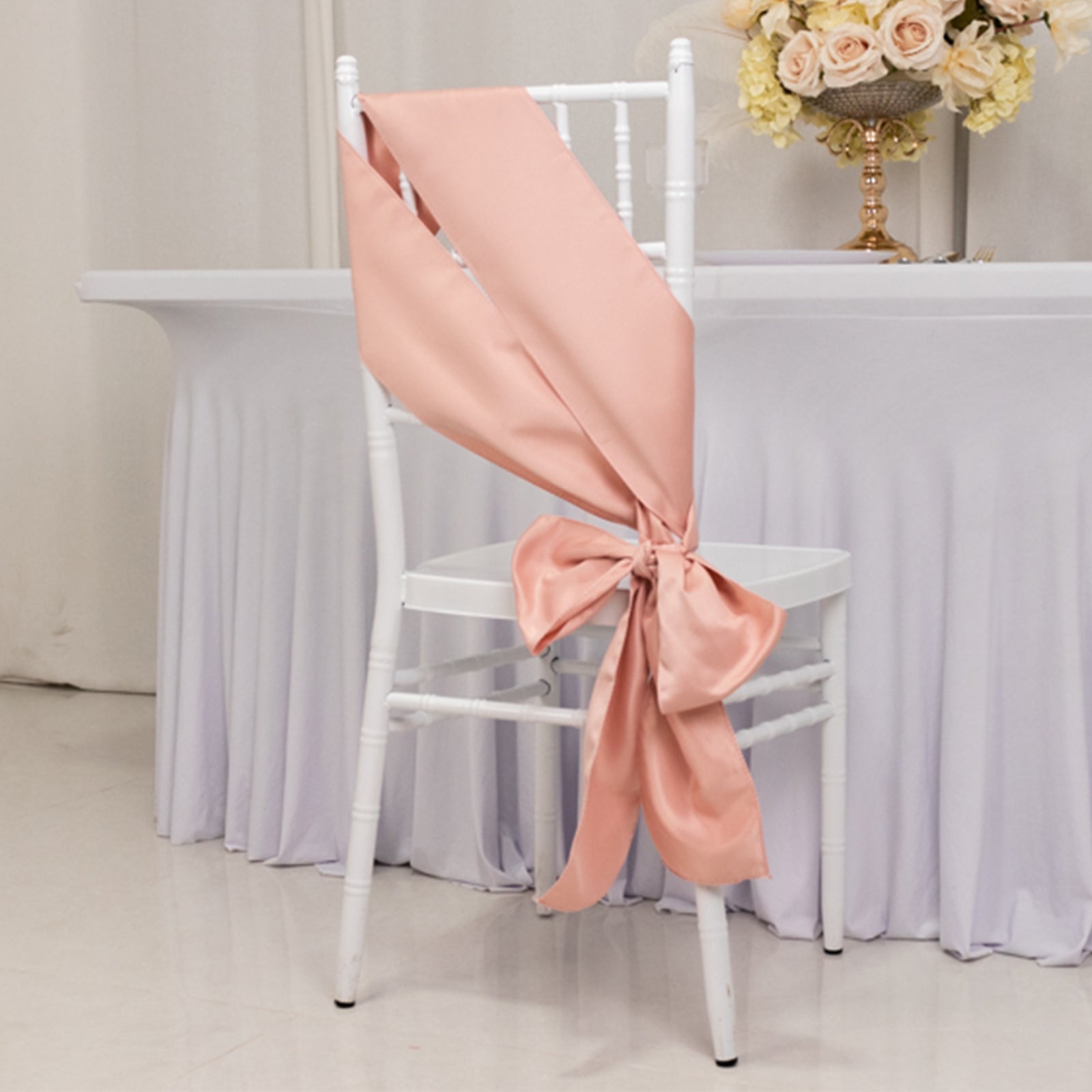 Dusty rose satin chair sash tied in a bow on a white chair.