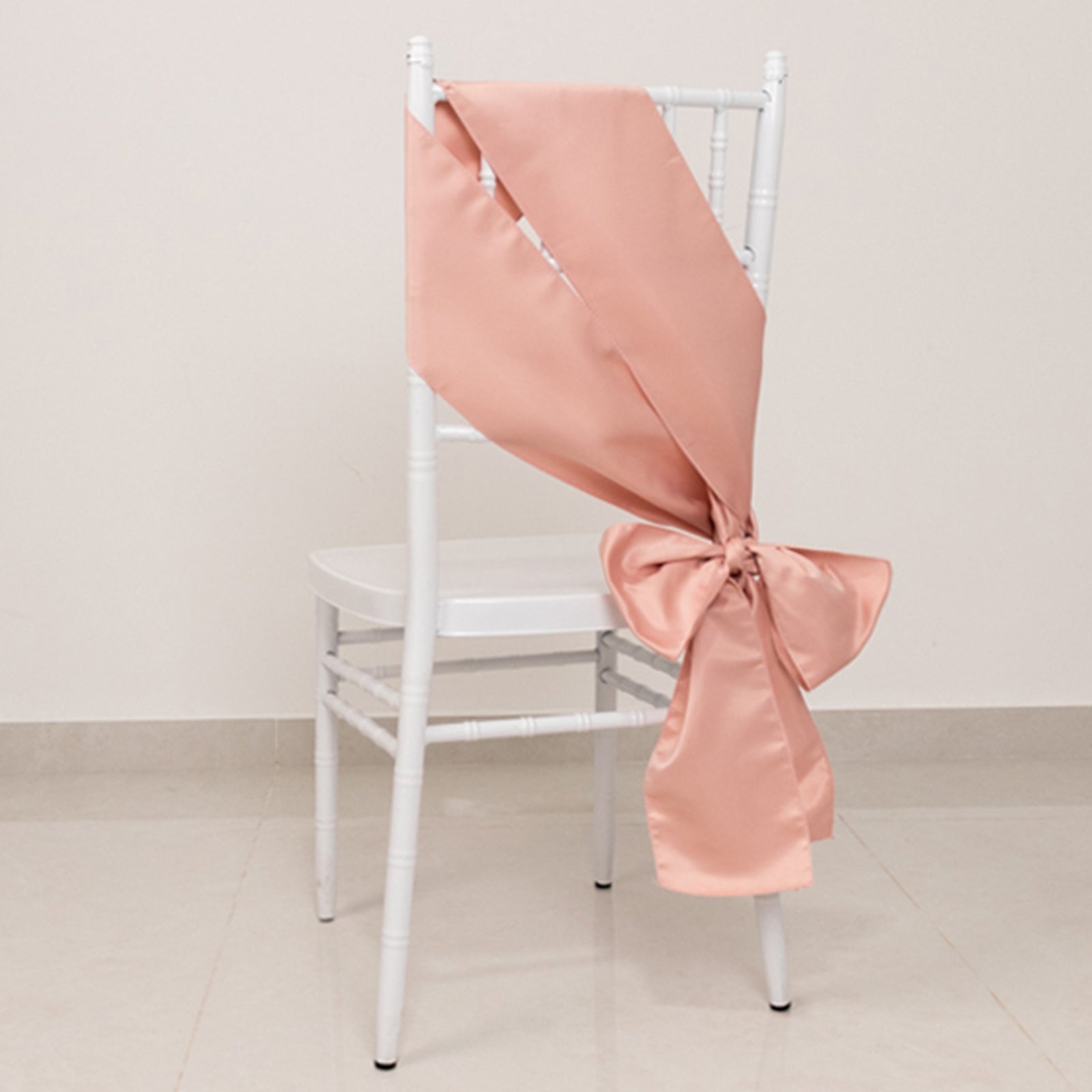 Dusty rose satin chair sash tied in a bow on a white chair.