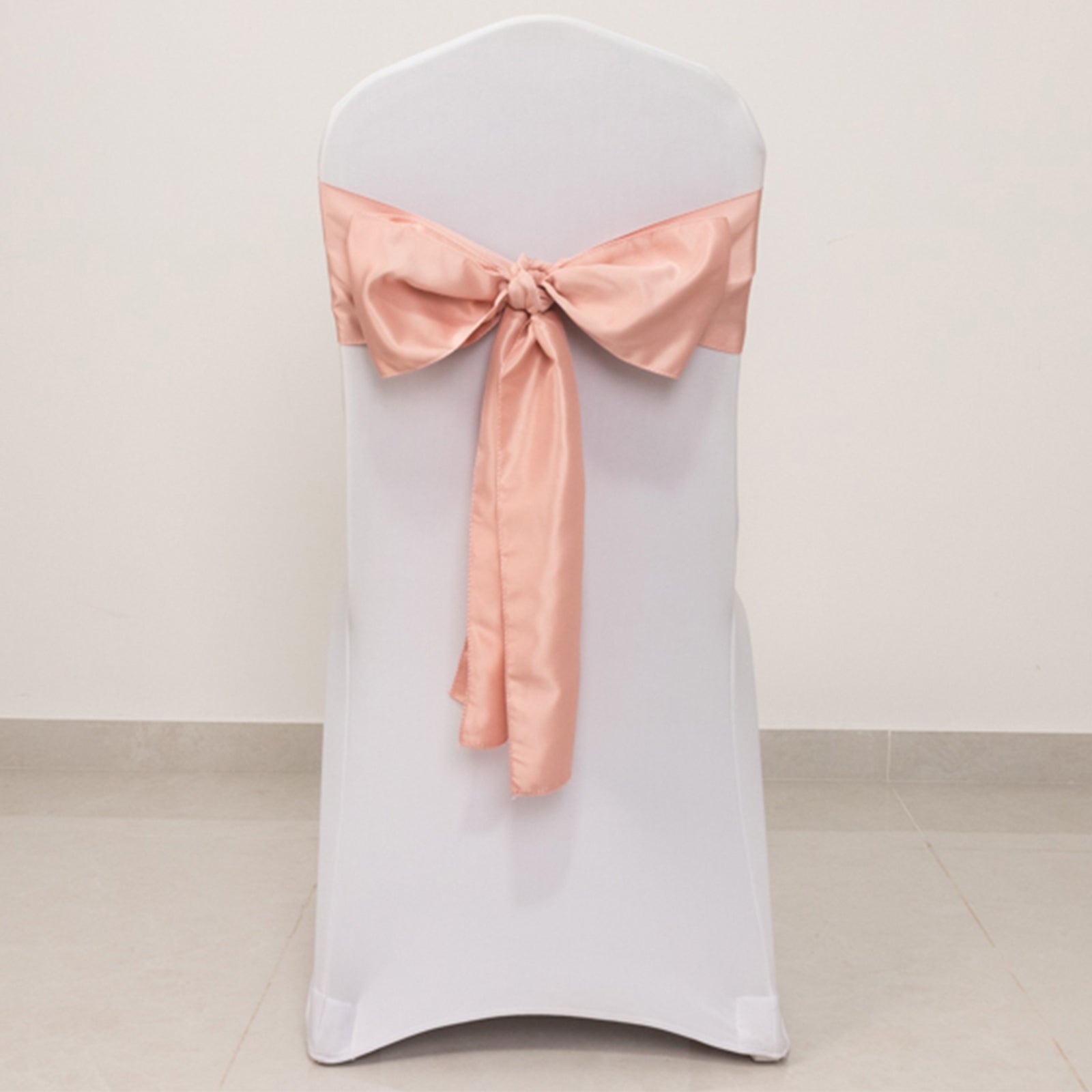 Dusty rose satin chair sash tied in a bow on a white chair.