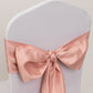 Dusty rose satin chair sash bow on a white chair.