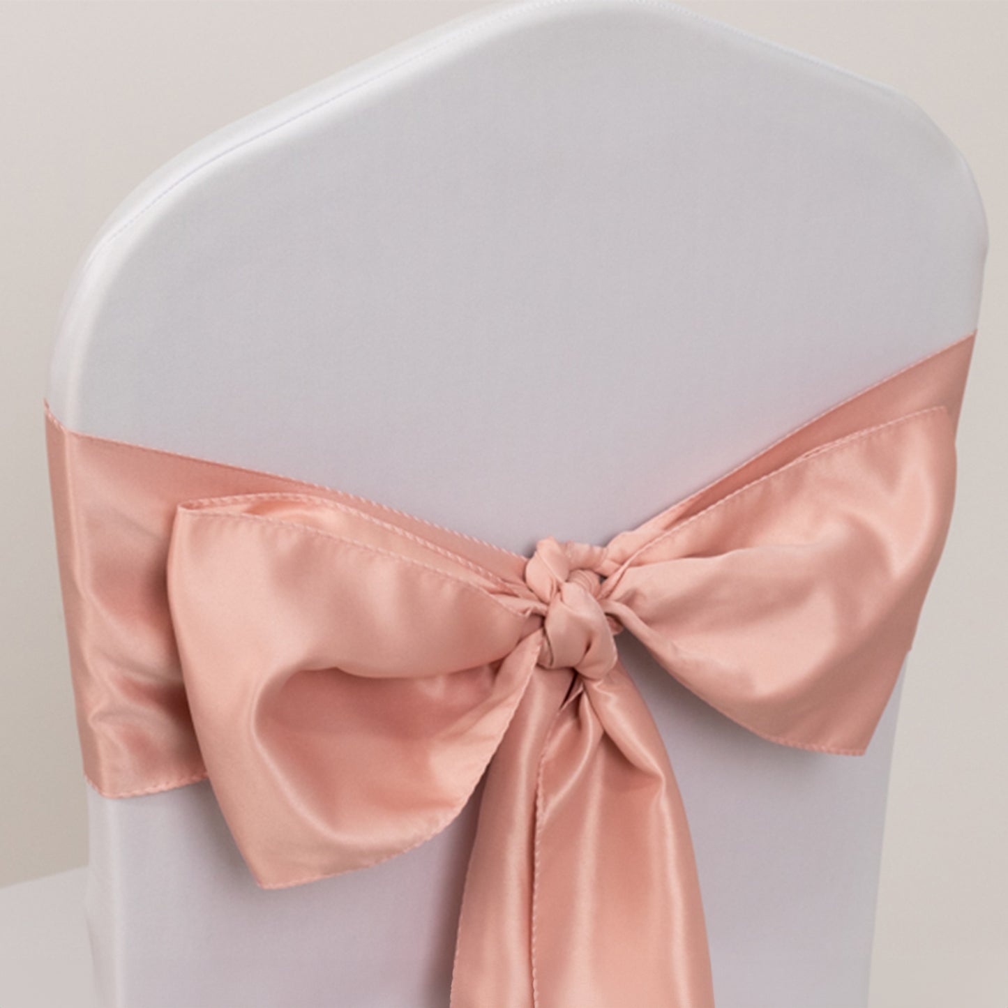 Dusty rose satin chair sash bow on a white chair.