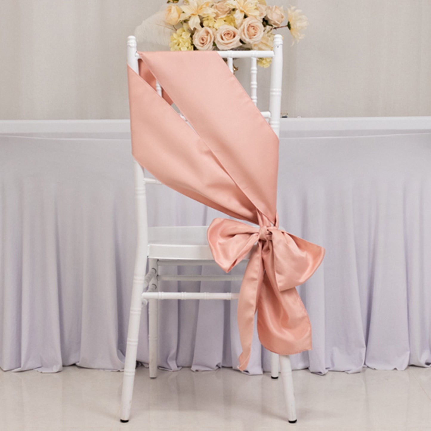 Dusty rose satin chair sash elegantly tied in a bow on a white chair.