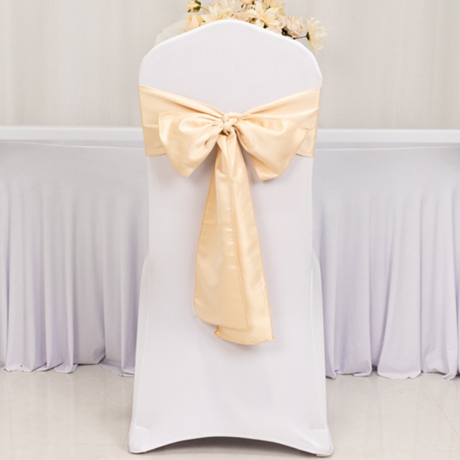 Beige satin chair sash bow on a white chair.