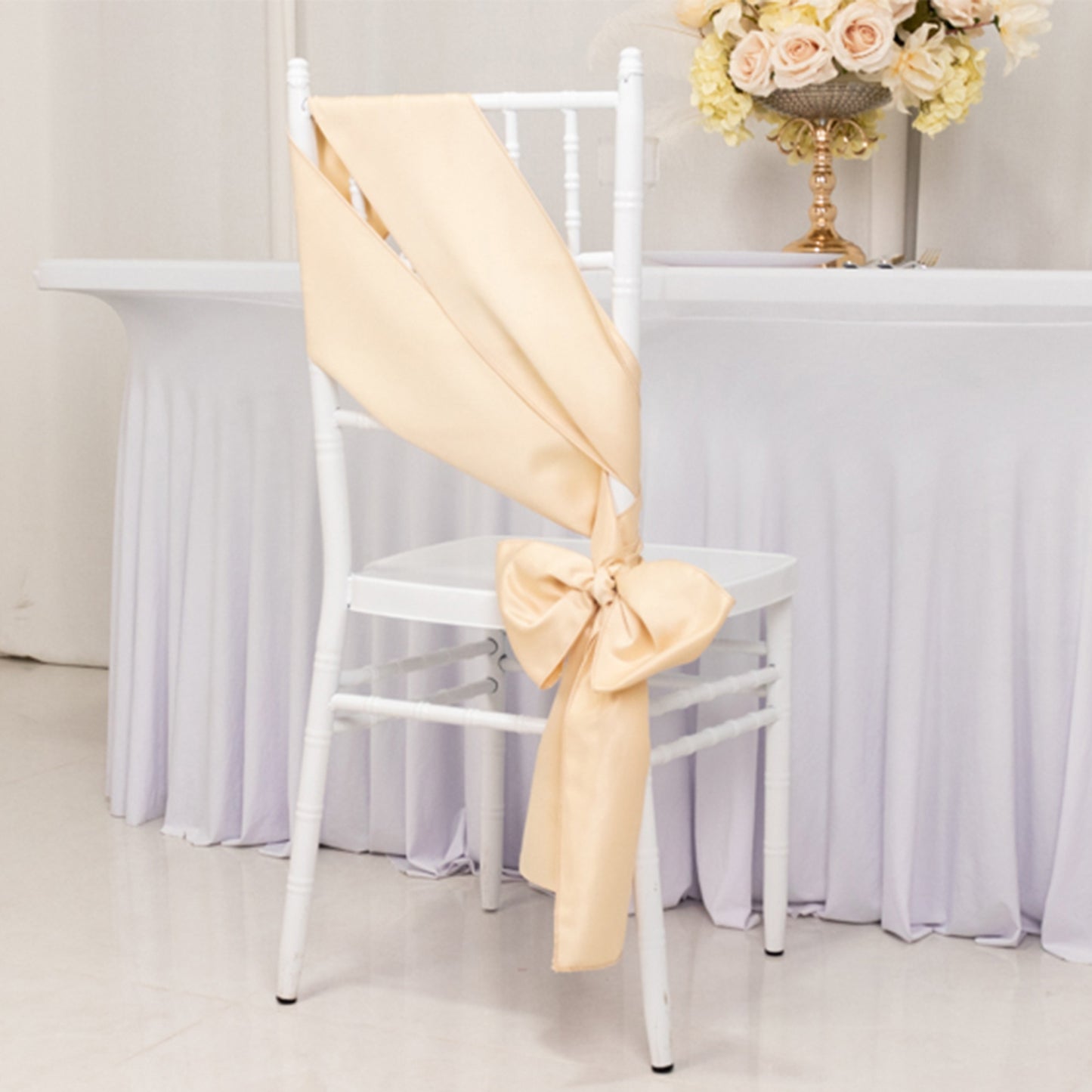 Beige satin chair sash with bow, elegantly draped on a white chair.