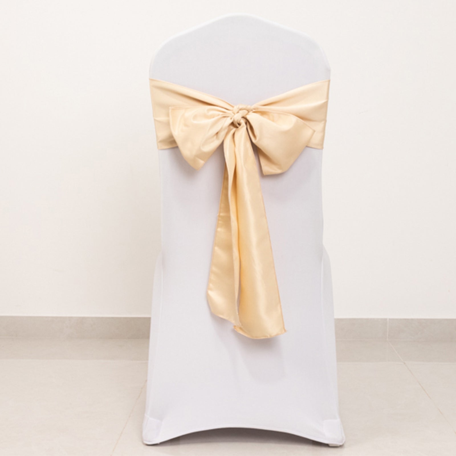 Beige satin chair sash with bow on a white chair.