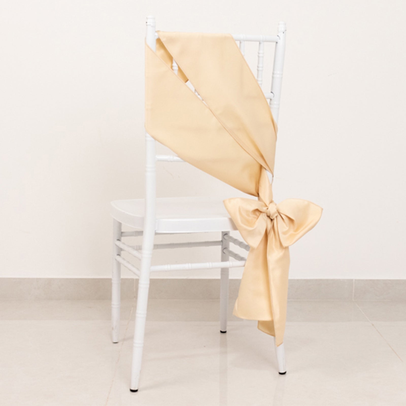 Beige satin chair sash with bow on a white chair.