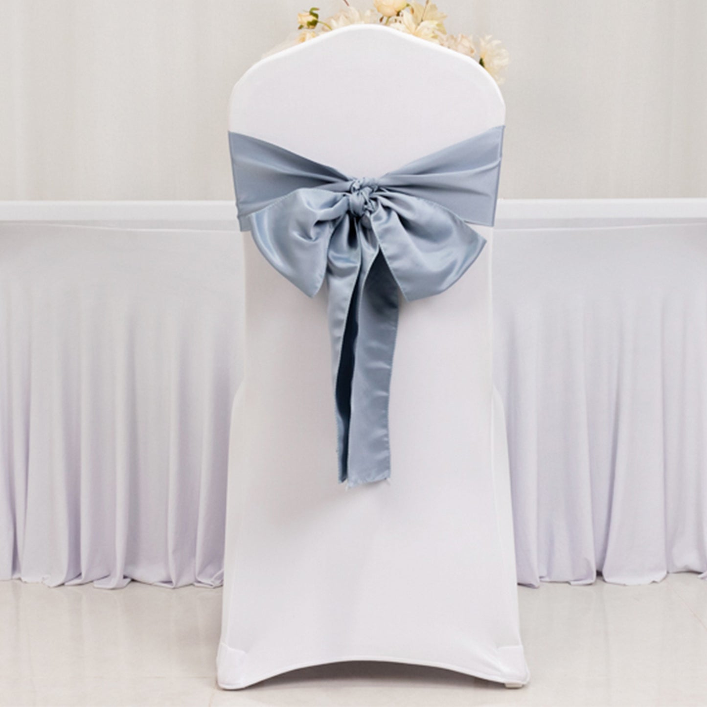 Dusty blue satin chair sash with bow on a white chair.