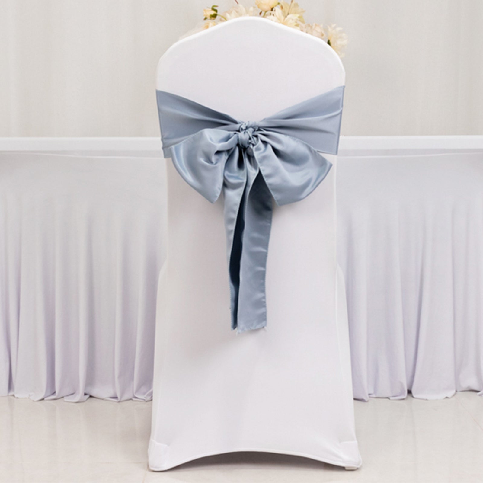 Dusty blue satin chair sash with bow on a white chair.