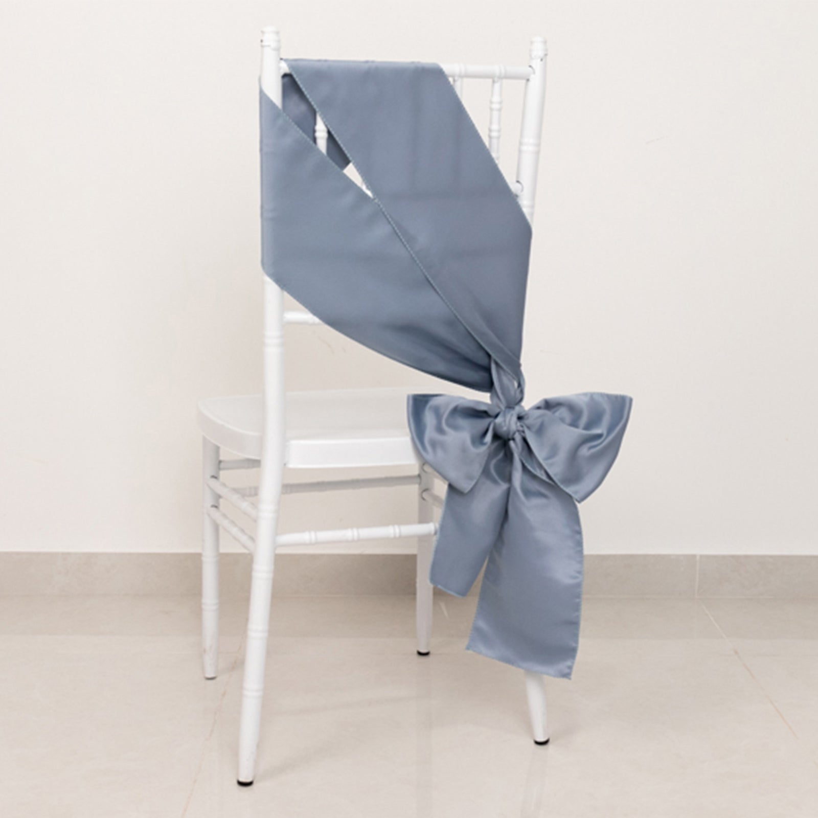 Dusty blue satin chair sash tied in a bow on a white chair.