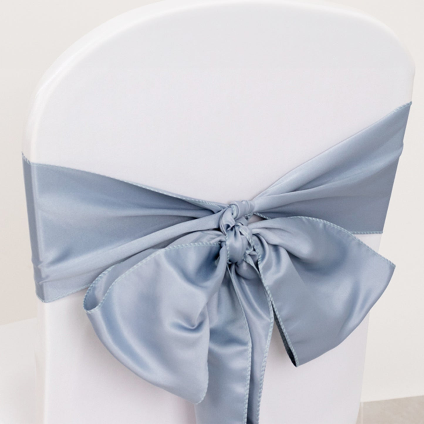 Dusty blue satin chair sash tied in a bow on a white chair.