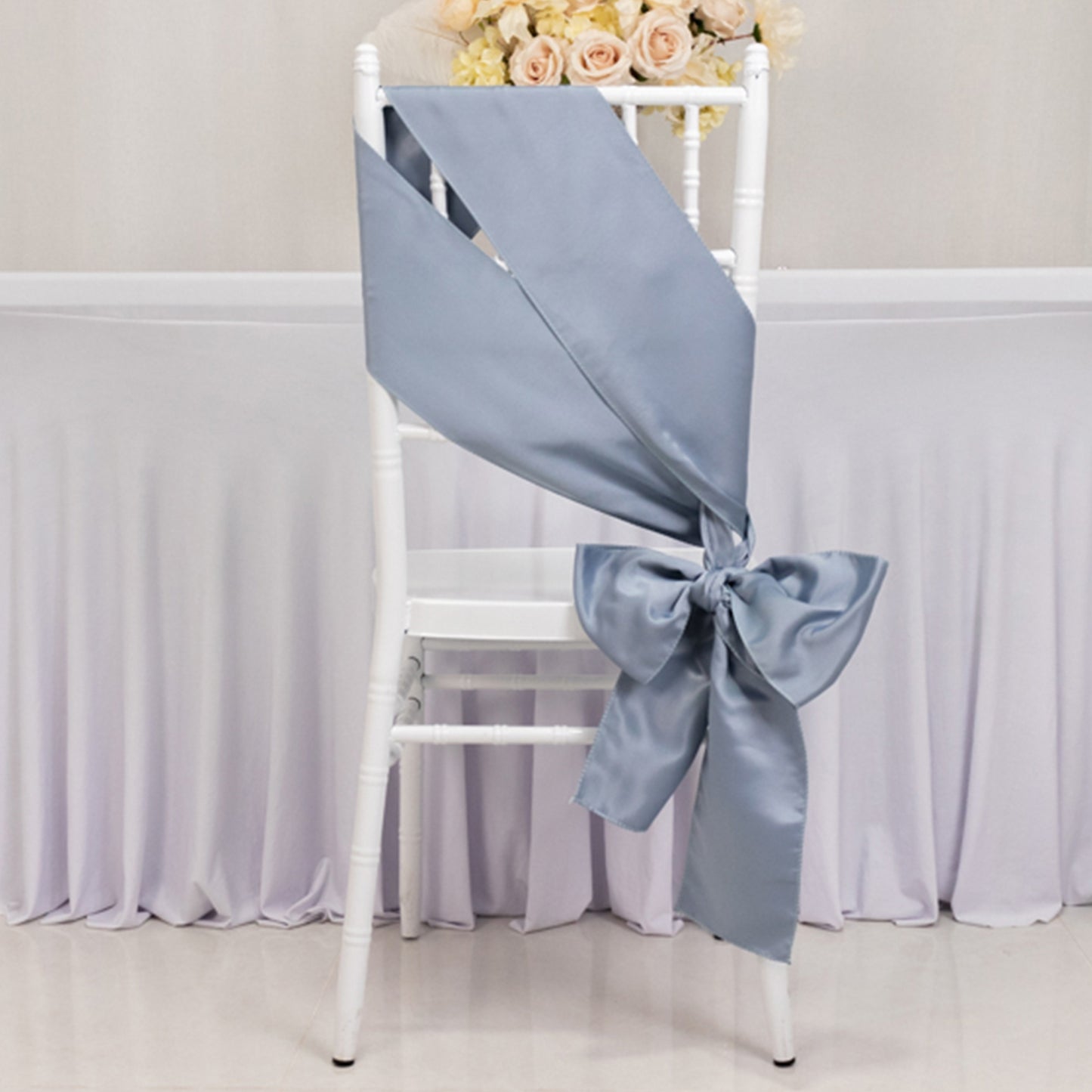 Dusty blue satin chair sash tied in a bow on a white chair.