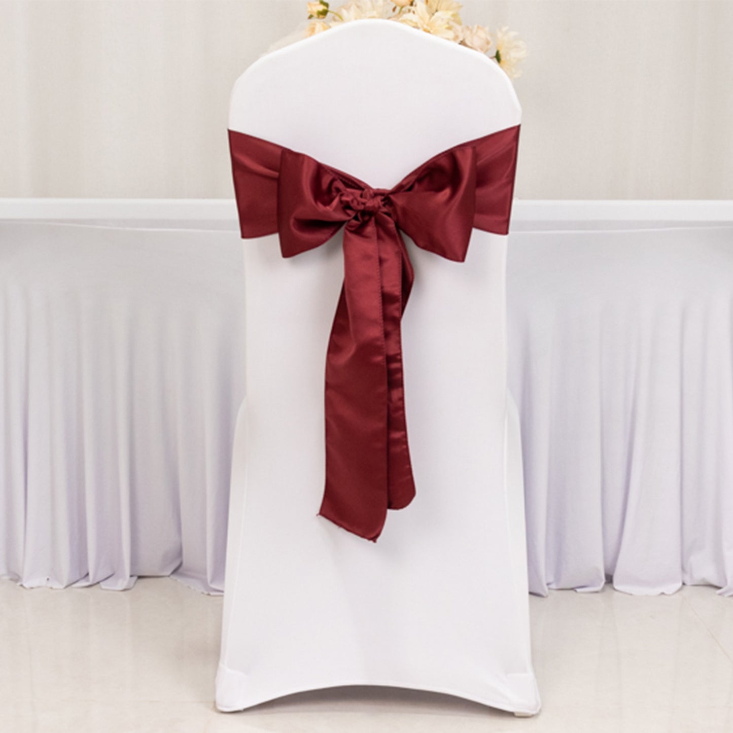 Burgundy satin chair sash elegantly tied on a white chair.