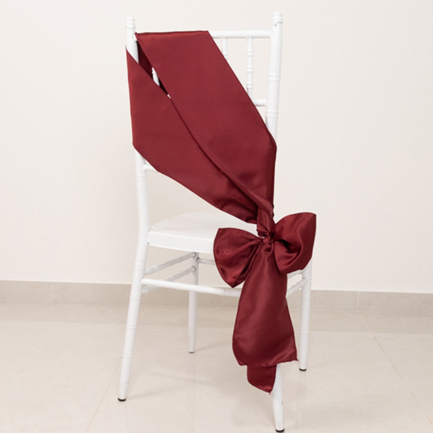 Burgundy satin chair sash elegantly tied in a bow on a white chair.