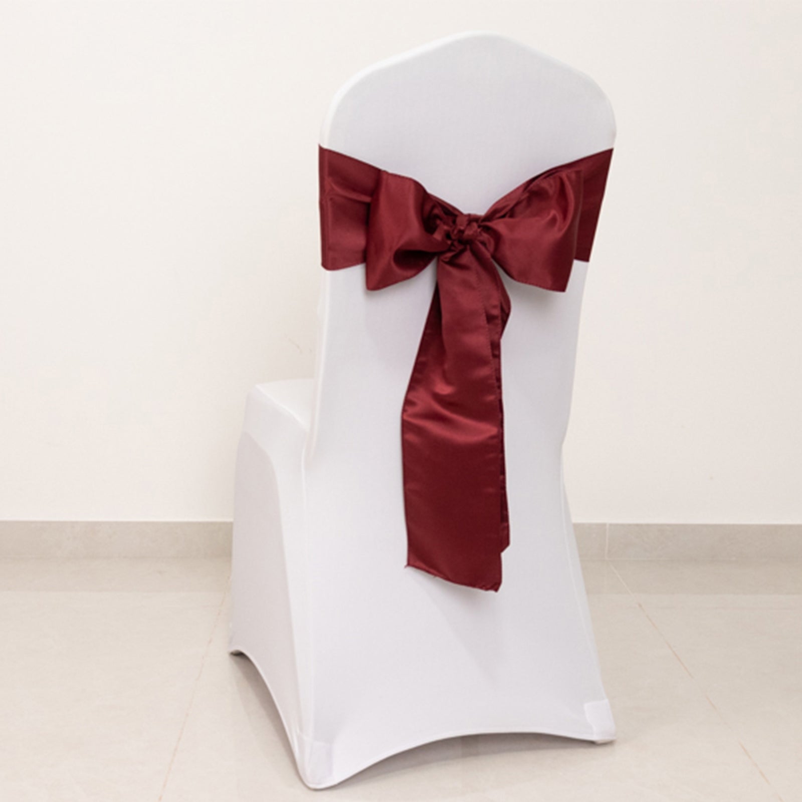Burgundy satin chair sash bow on a white chair.