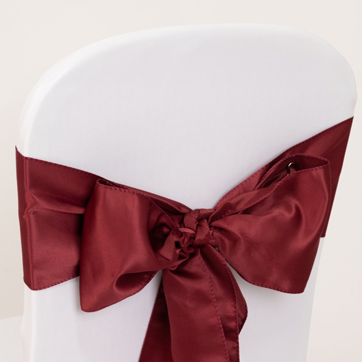 Burgundy satin chair sash bow on a white chair.