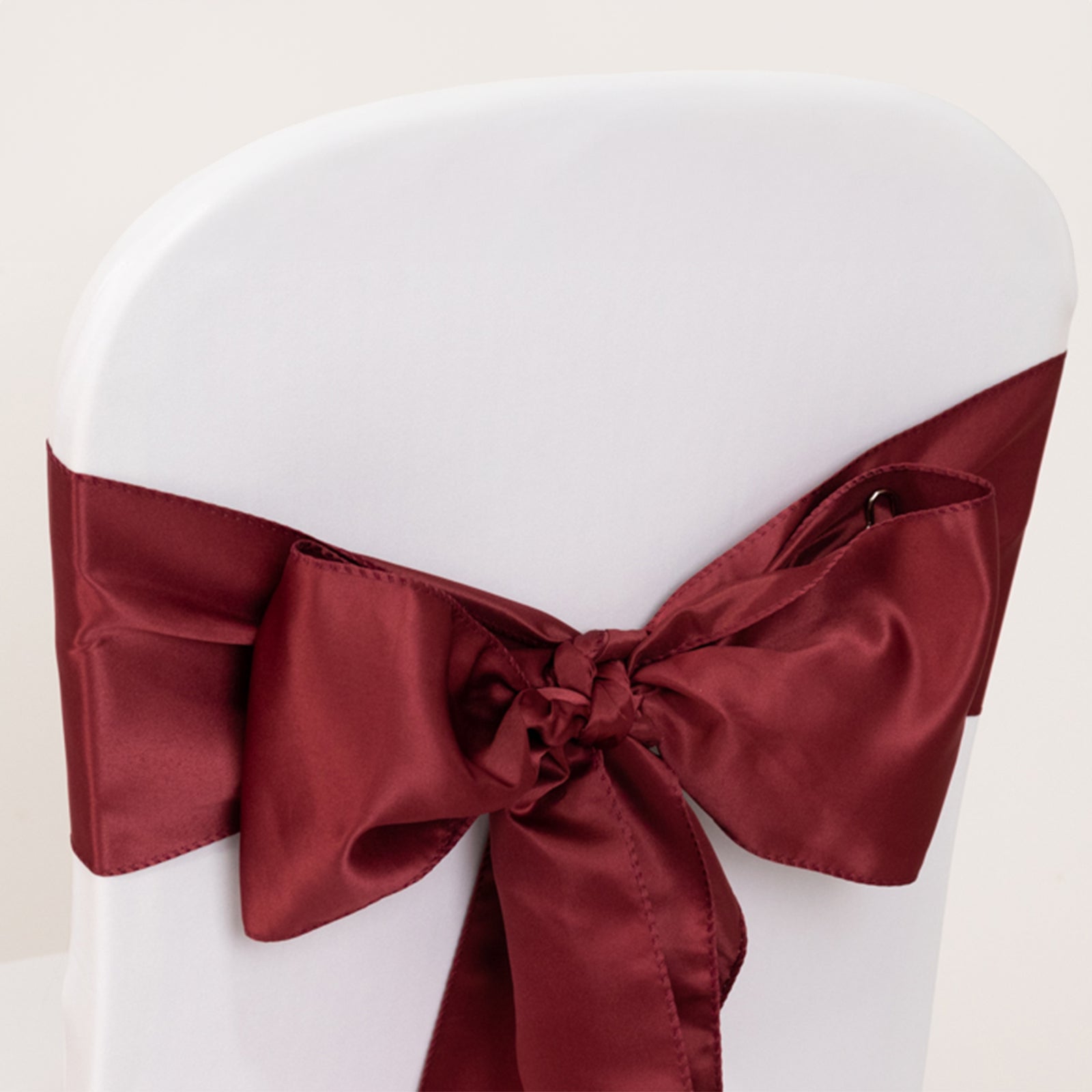 Burgundy satin chair sash bow on a white chair.