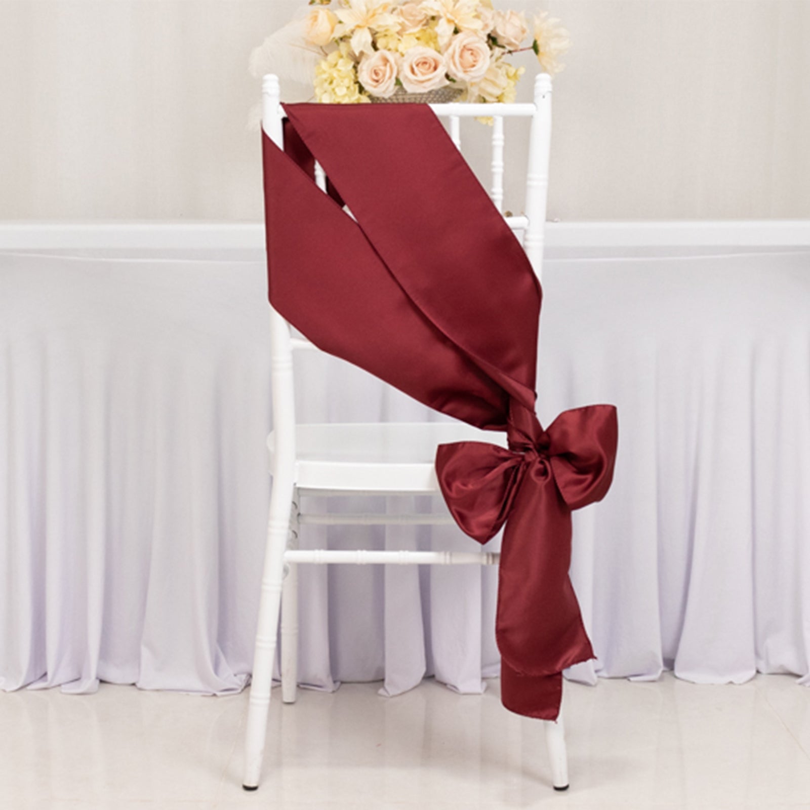 Burgundy satin chair sash with bow on a white chair.