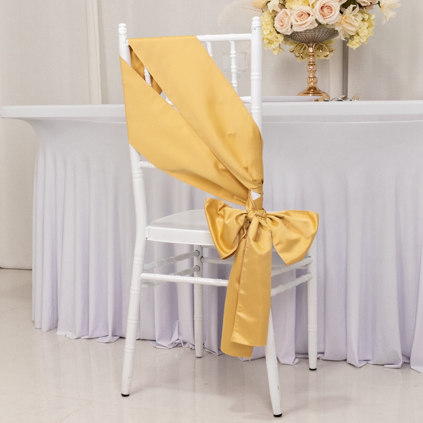 Champagne satin chair sash bow on a white chair at an event setup.