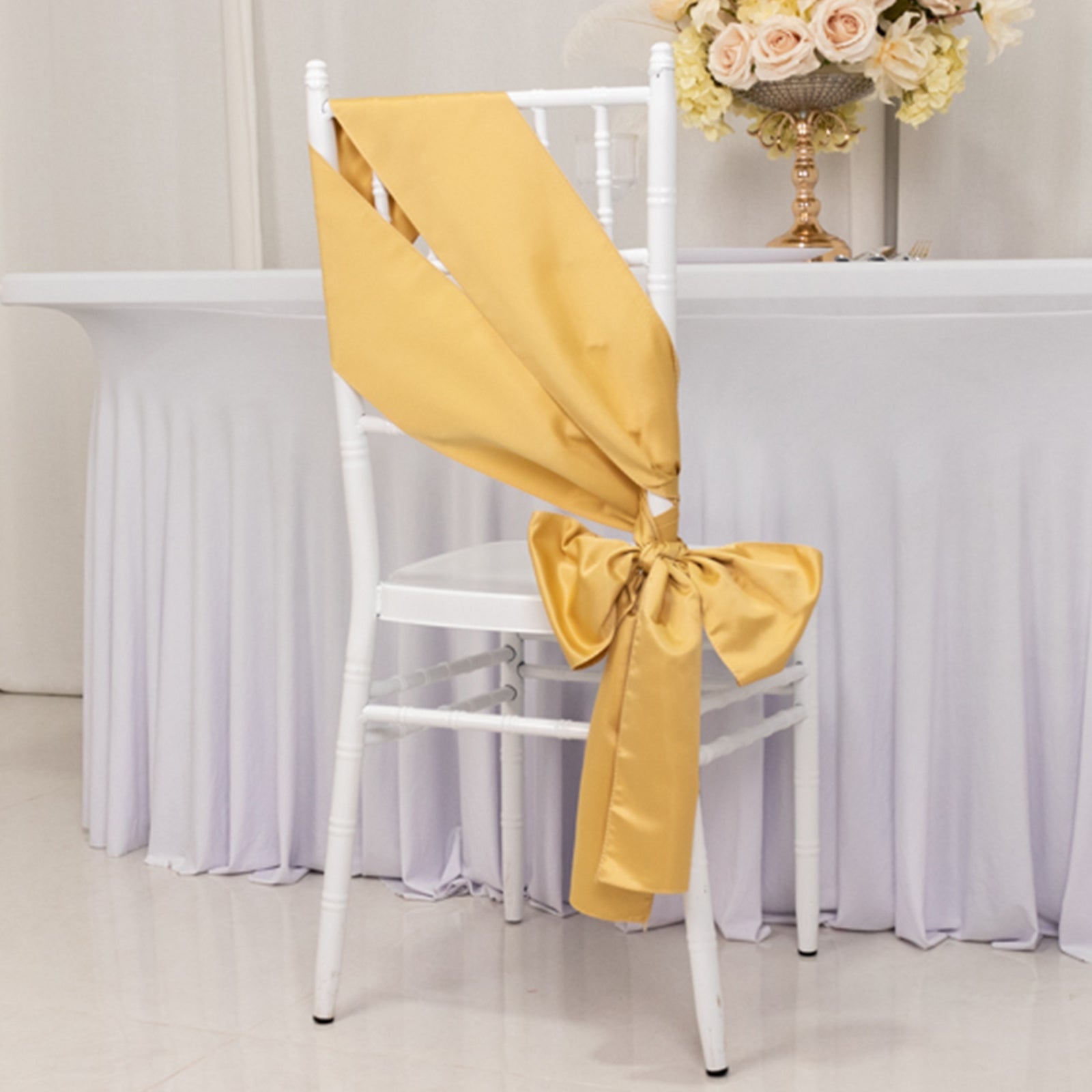 Champagne satin chair sash bow on a white chair at an event setup.
