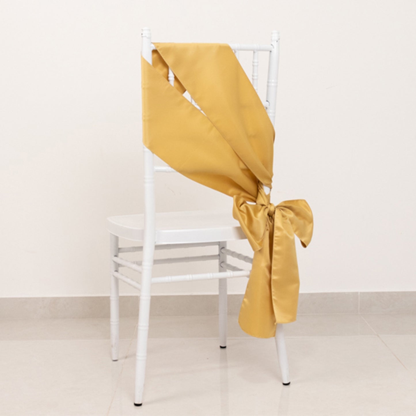 Champagne satin chair sash tied in a bow on a white chair.