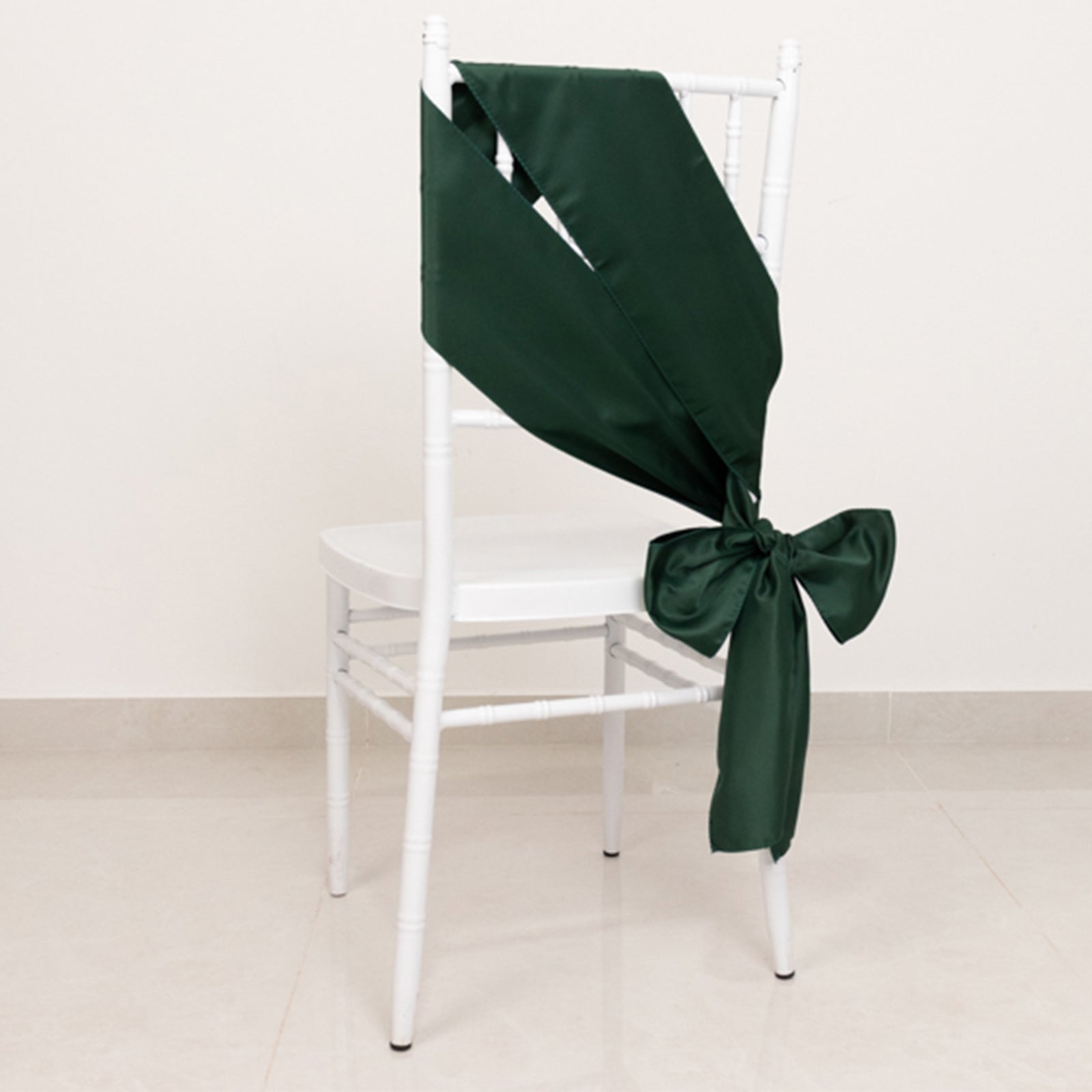 Emerald green satin chair sash tied in a bow on a white chair.